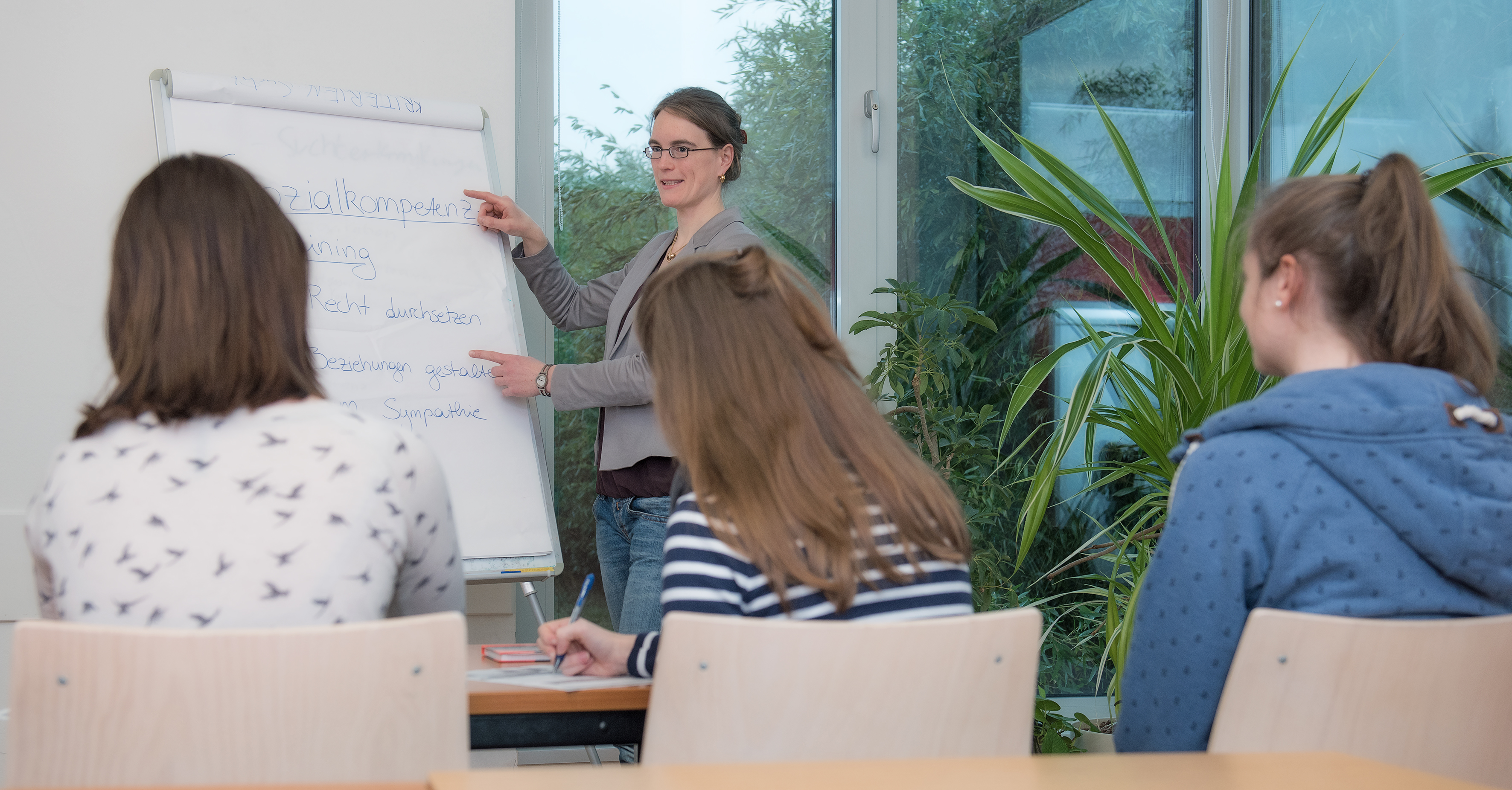 Frau am Flipchart erkärt drei Zuhörerinnen etwas über Sozialkompetenz