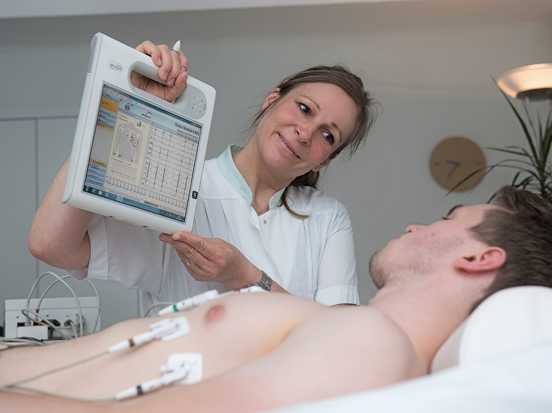 Frau in weißem Kittel erklärt Patienten an einer Tafel die Behandlung