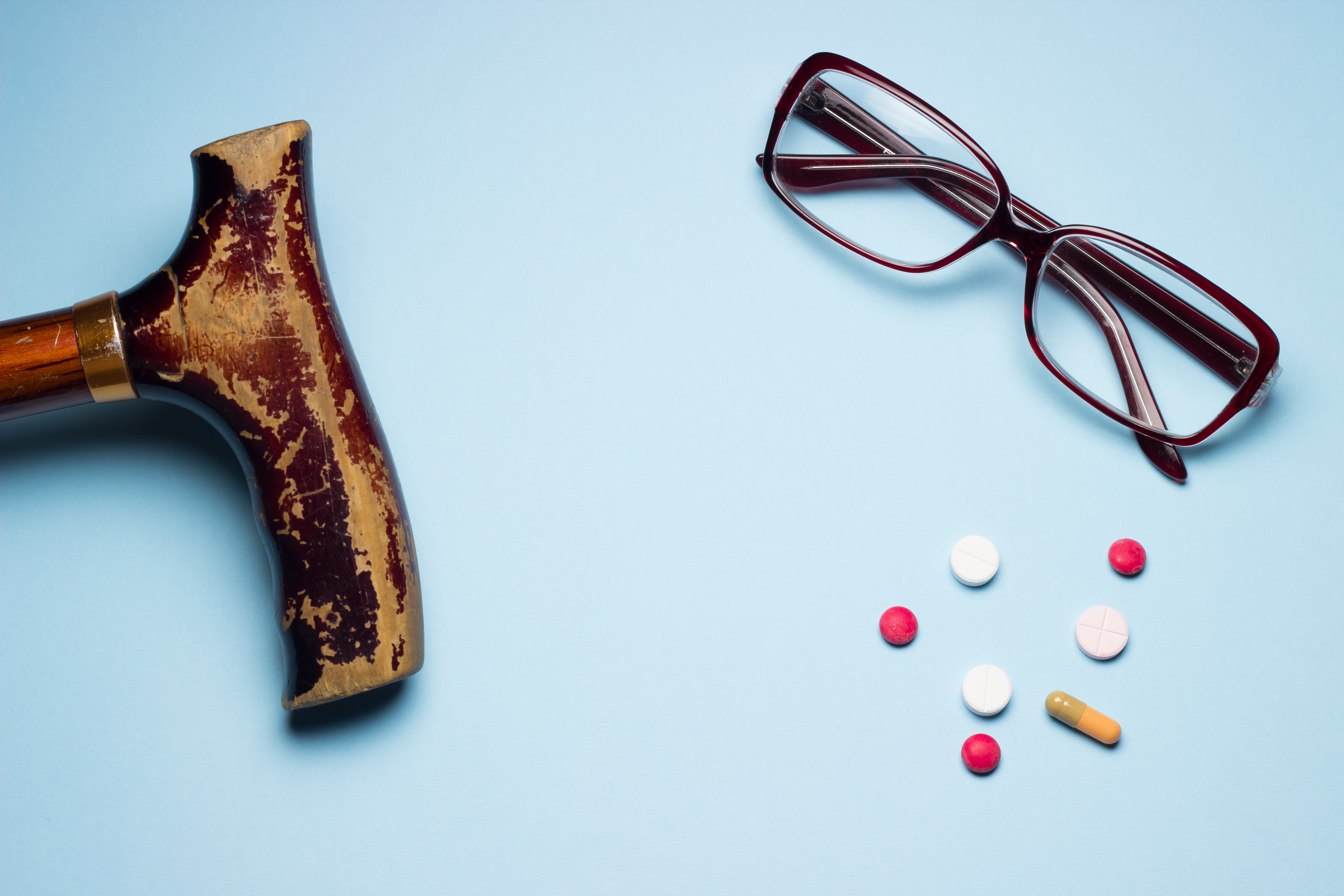 Gehstock, Tabletten und Brille liegen auf blauem Untergrund