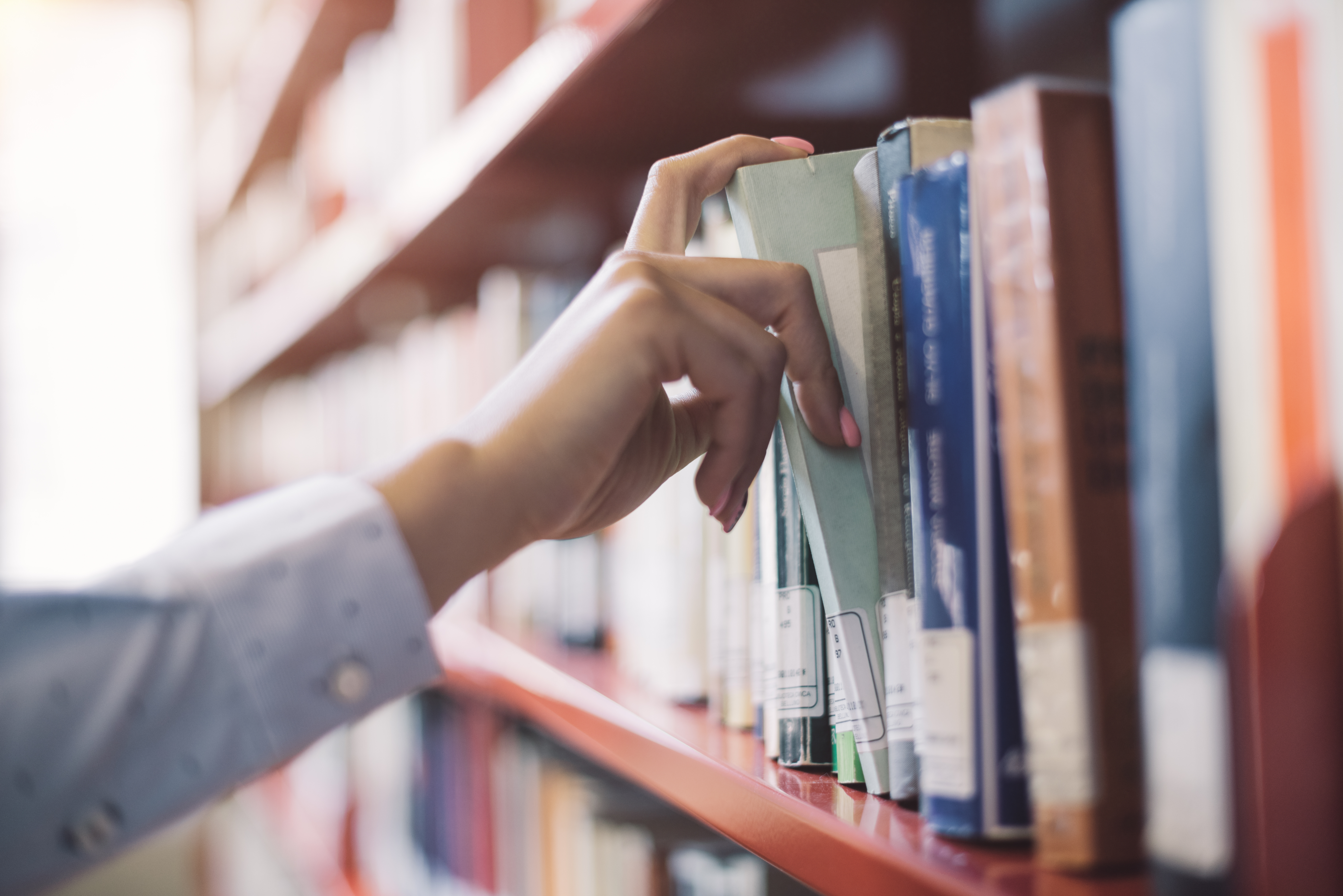 Ein Mensch nimmt ein Buch aus einem Bücherregal, ist es eine Hand zu sehen