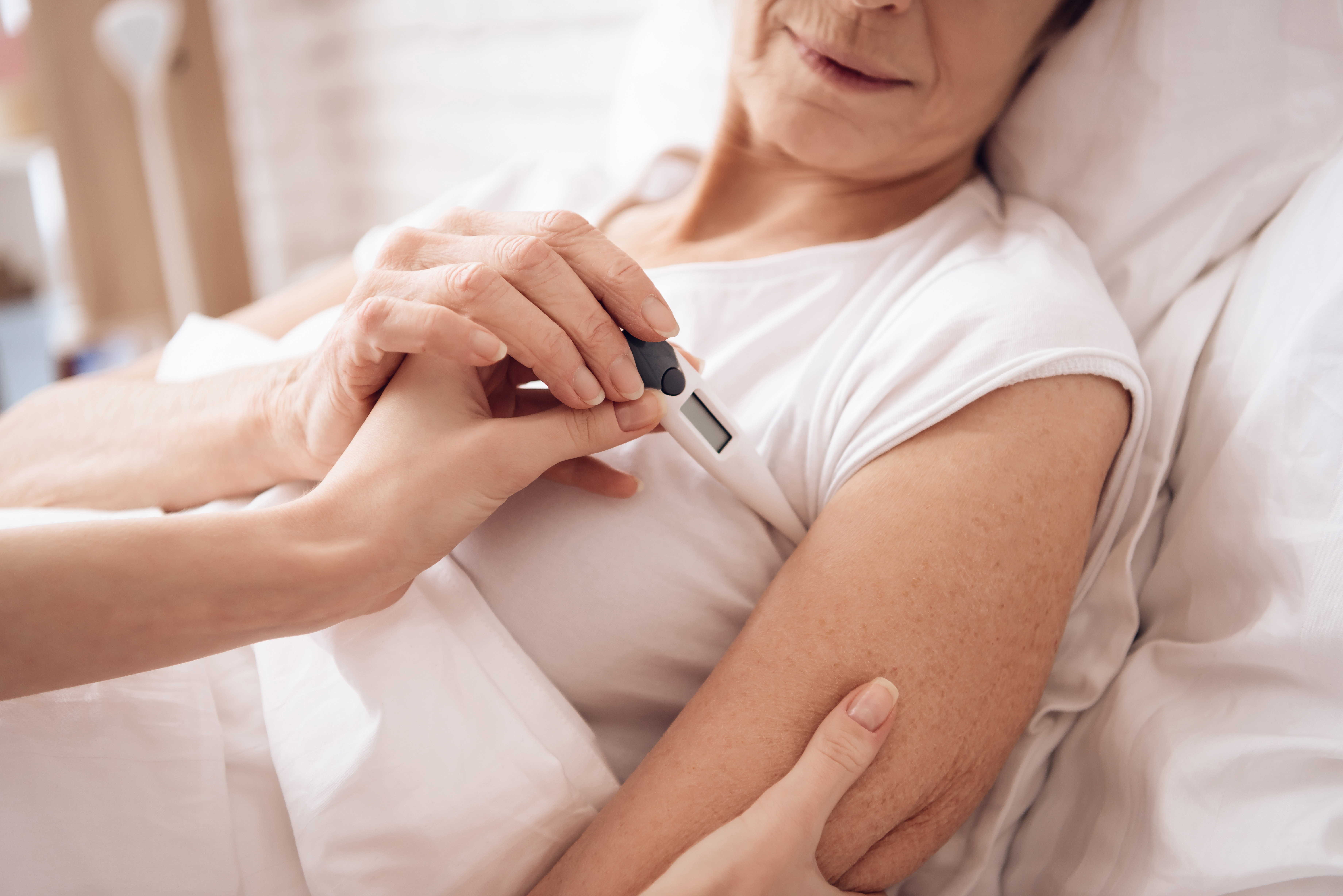 Eine Person misst bei einer liegenden Frau mit einem Fieberthermometer in der Achselhöhle die Temperatur