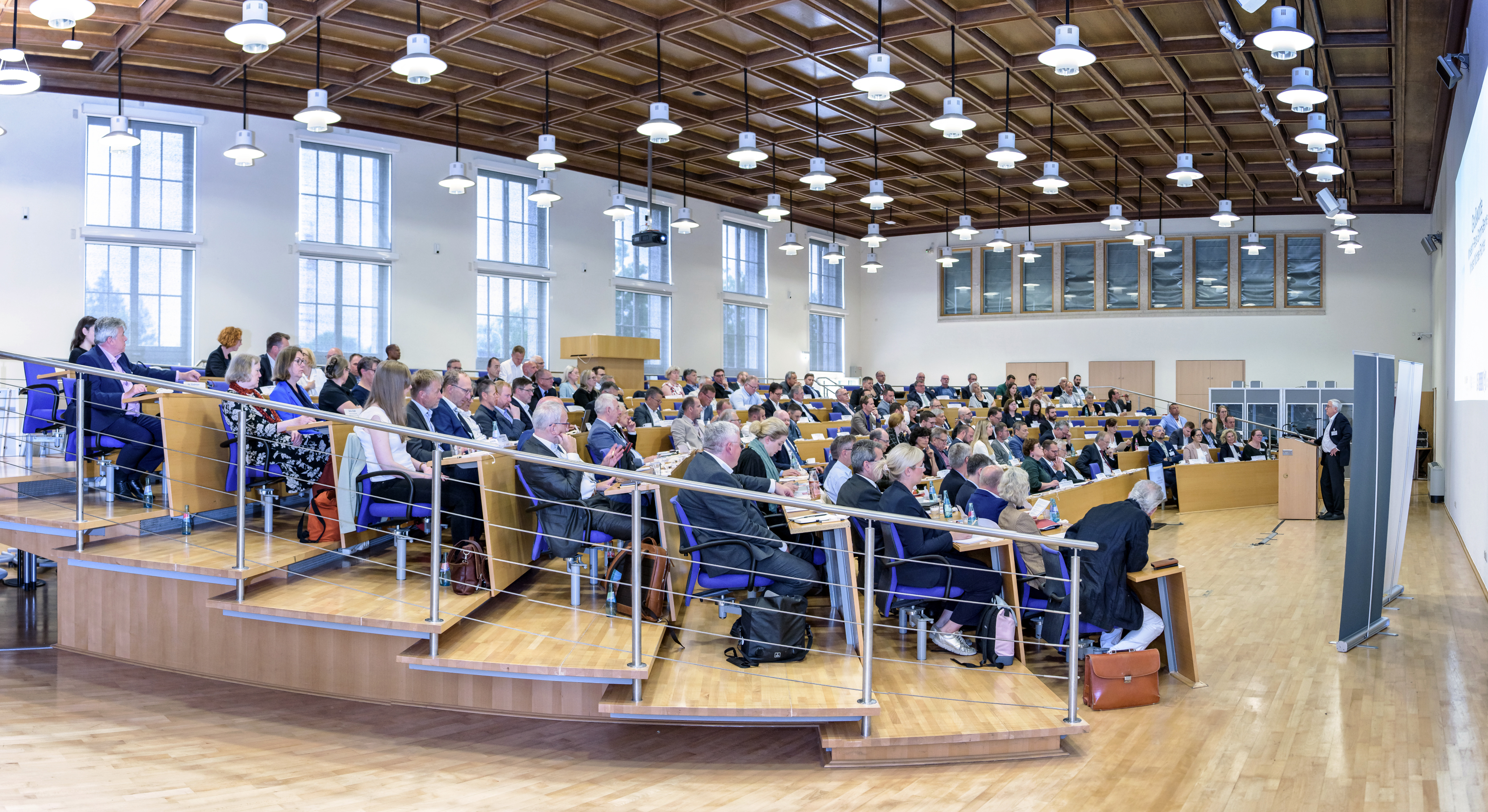 Panoramaansicht eines Plenums mit Redner am Pult auf der rechten Seite