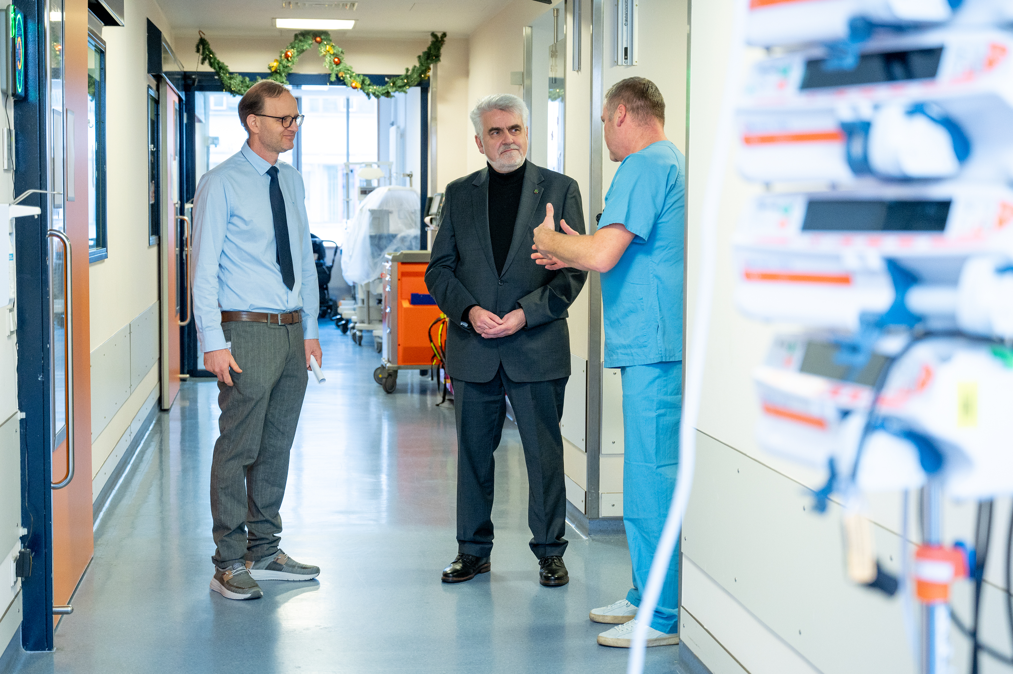 Drei Männer in einem Krankenhausflur im Gespräch.