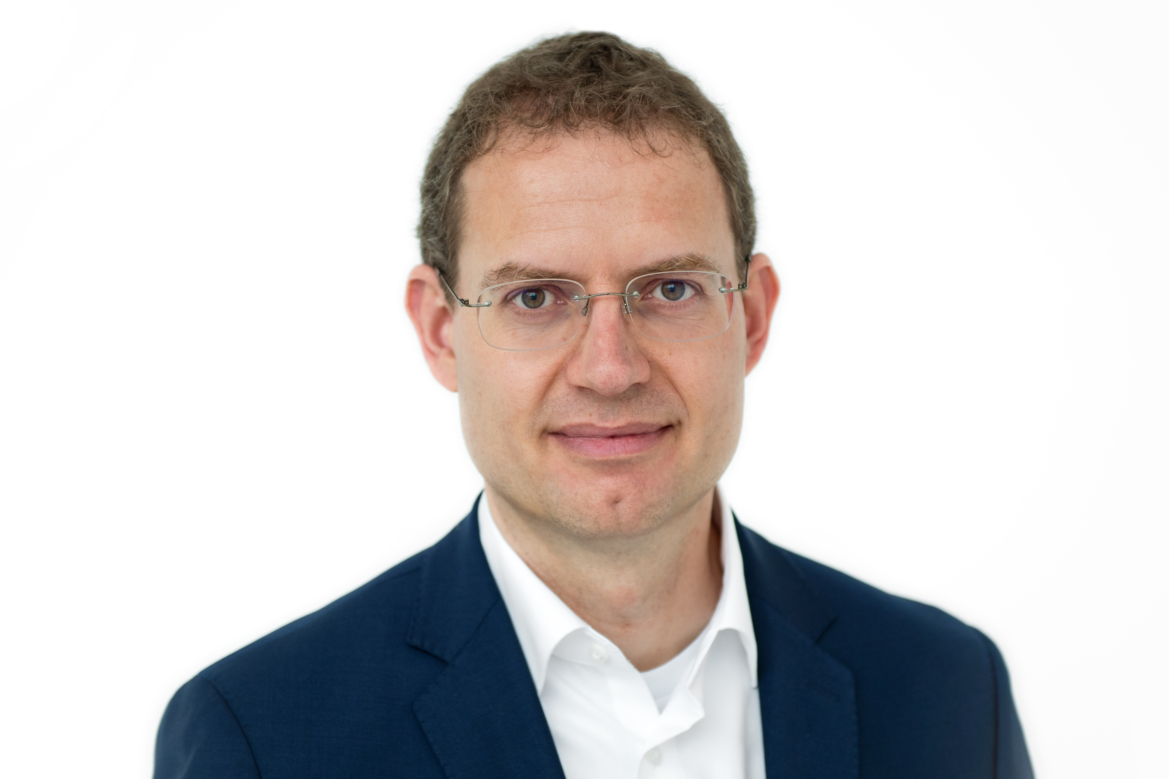 Ein Mann mit randloser Brille und kurzen, leicht gelockten braunen Haaren lächelt in die Kamera.