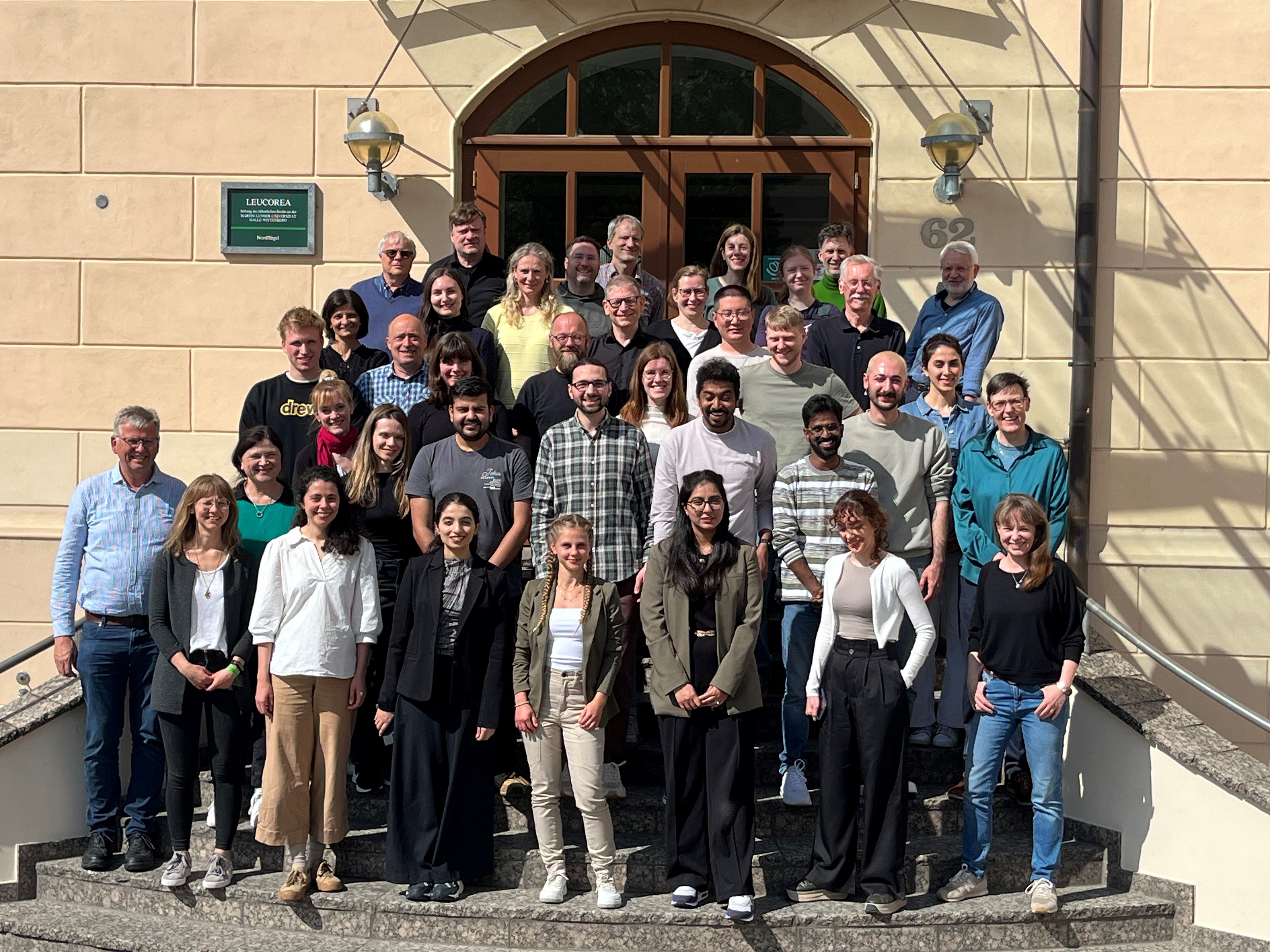 Für ein Gruppenfoto stehen knapp 40 Personen auf einer Treppe vor der Leucora in Wittenberg. Die Sonne scheint ihnen ins Gesicht.