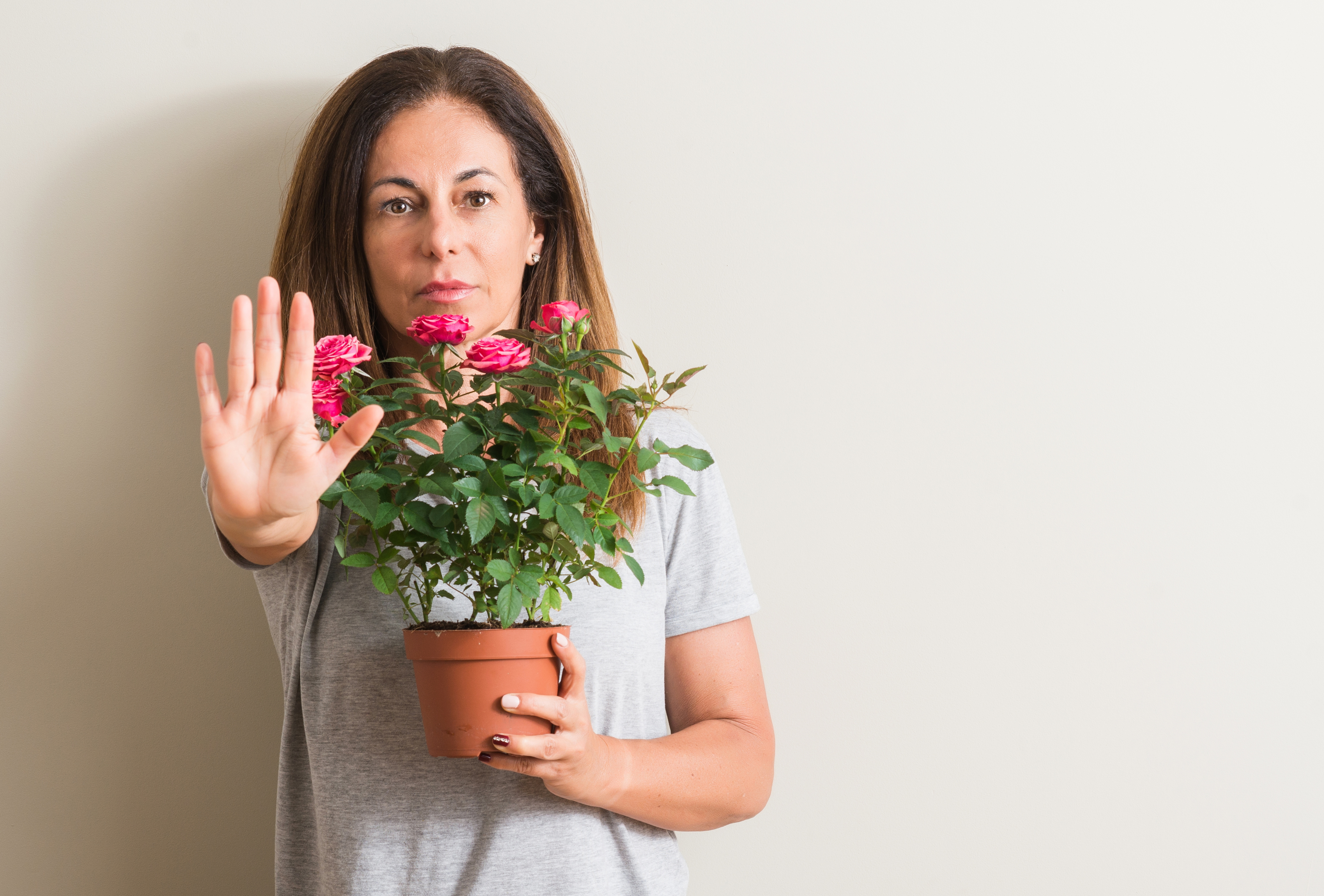 Eine Frau hält einen Blumentopf vor ihrem Körper und zeigt mit der Hand das Stopp-Zeichen - Symbol für kein Blumentopf