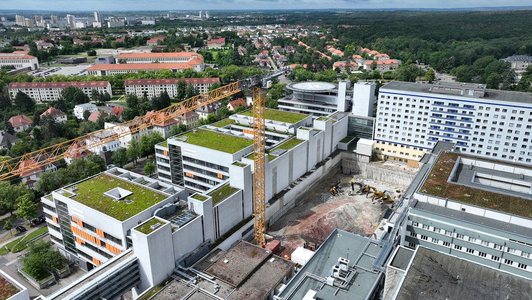 Luftaufnahme eines Ausschnitts des Klinikgeländes. Links, oben rechts und rechts befinden sich Gebäude des Universitätsklinikums Halle (Saale). Die Baugrube befindet sich zentral zwischen den Gebäuden.