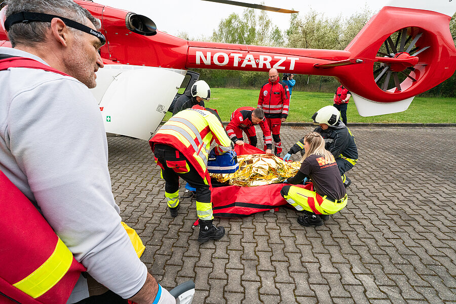 Rettungsteam versorgt verletzte Person neben einem Notarzthubschrauber auf einem Parkplatz. Rettungsteam versorgt verletzte Person neben einem Notarzthubschrauber auf einem Parkplatz.