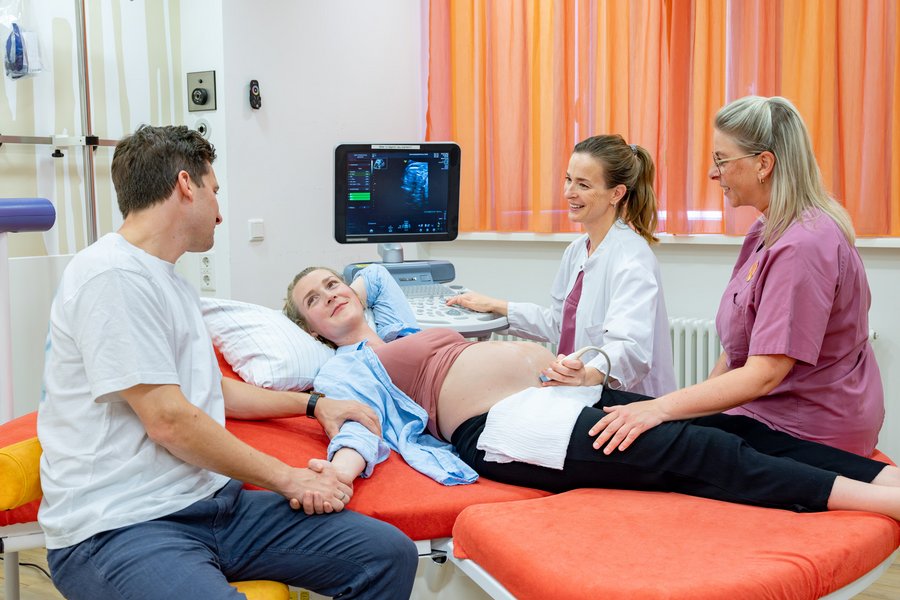 Eine Schwangere auf einer Liege wird mit Ultraschall von einer Ärztin untersucht. Eine Hebamme und ein Mann sitzen an der Liege. Eine Schwangere auf einer Liege wird mit Ultraschall von einer Ärztin untersucht. Eine Hebamme und ein Mann sitzen an der Liege.
