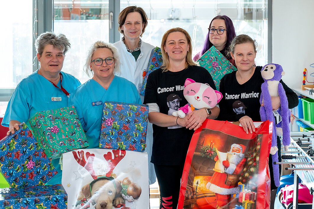 Drei Vertreterinnen des Vereins Cancer Warrior Eisleben und drei Mitarbeitende des UKH posieren für ein Gruppenfoto. Einige Personen halten Geschenke in den Händen.