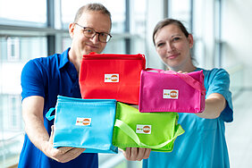 Zwei Personen halten vier Kühltaschen in die Kamera. Die Kühltaschen stehen im Fokus, die Personen sind unscharf.