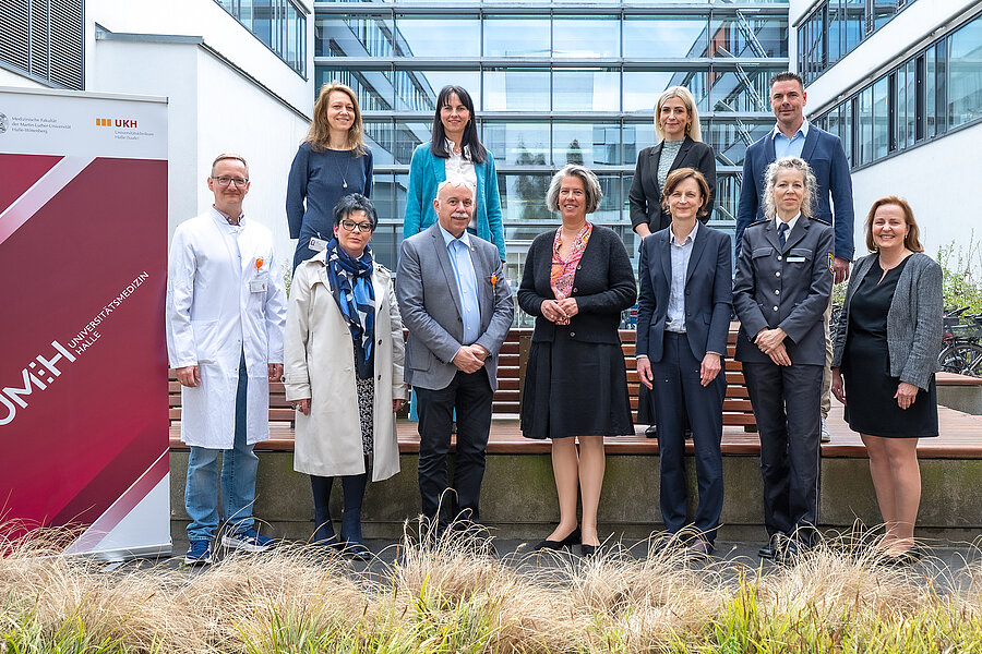 Gruppenbild von mehreren Personen auf dem Gelände des Universitätsklinikums Halle (Saale). Links im Bild steht ein Roll-up der Universitätsmedizin Halle. Die hintere Reihe der Gruppe steht etwas erhöht. Gruppenbild von mehreren Personen auf dem Gelände des Universitätsklinikums Halle (Saale). Links im Bild steht ein Roll-up der Universitätsmedizin Halle. Die hintere Reihe der Gruppe steht etwas erhöht.