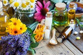 Kräutersalze und Öle in kleinen Glasfläschchen inmitten von Blumen