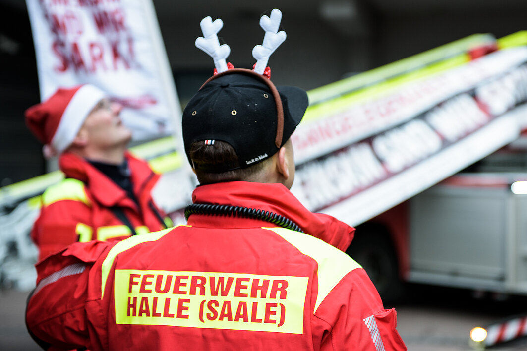 Ein Mitarbeiter der Feuerwehr in Arbeitskleidung trägt einen Haarreif mit einem Elchgeweih.