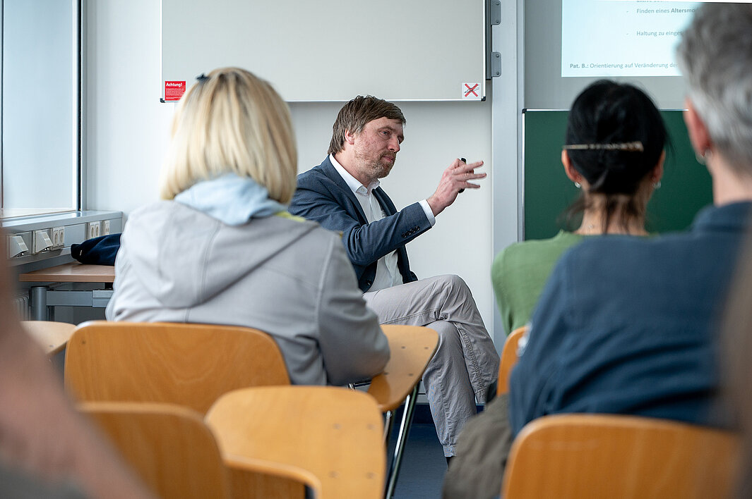 Momentaufnahme aus einem Workshop beim Geriatrietag 2026 der Universitätsmedizin Halle. Einige Personen sitzen mit dem Rücken zur Kamera in einem Seminarraum. Vorn sitzt die Person, die den Workshop durchführt und erklärt etwas.
