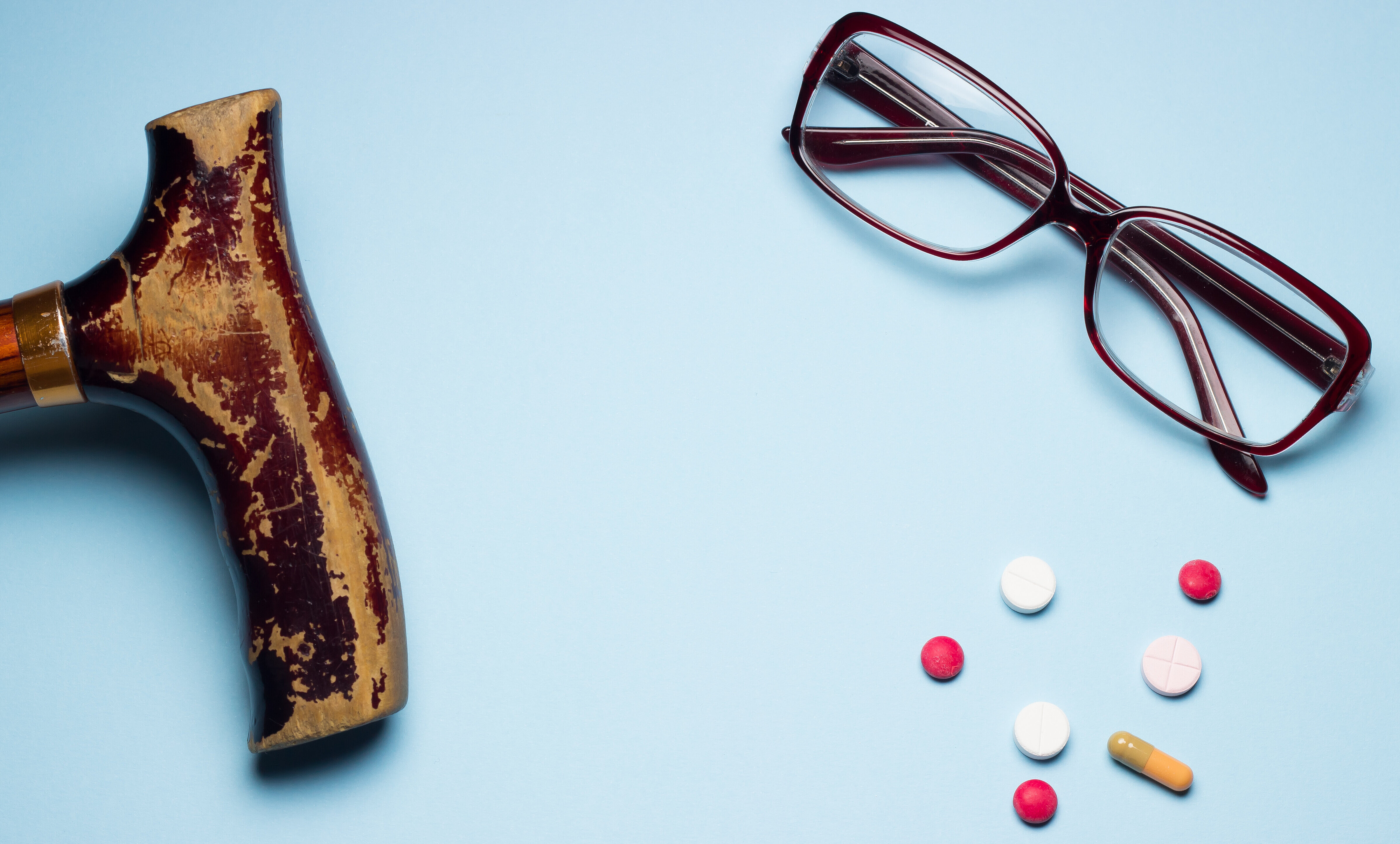 Gehstock, Tabletten und Brille liegen auf blauem Untergrund