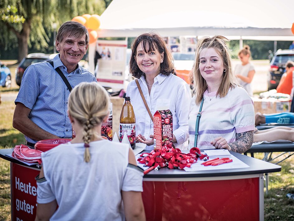 Drei Personen stehen auf der Ziegelwiese in Halle hinter einem Infostand. Davor steht ein Kind mit dem Rücken zur Kamera.