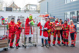 Gruppenfoto mit vier Männern in Höhenretter-Uniform mit Helmen und zwei Männern, die als Grinch und als Weihnachtsmann verkleidet sind.