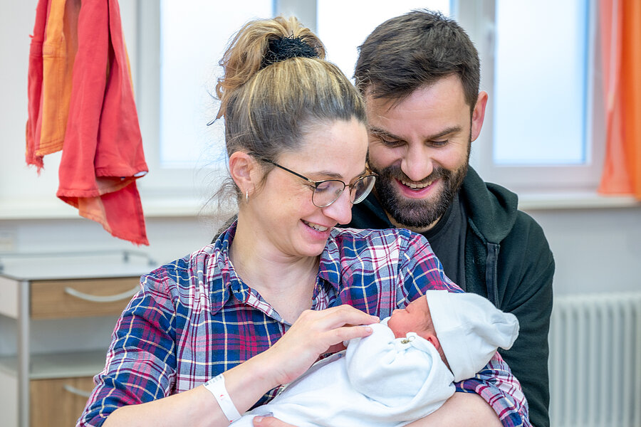 Mutter und Vater schauen lächelnd ihr neugeborenes Baby an.  Mutter und Vater schauen lächelnd ihr neugeborenes Baby an.