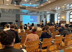 Ein Blick in den Konferenzsaal der Leucora in Wittenberg. Im Hintergrund wird eine Präsentation an die Wand projiziert. Rund 40 Personen hören dem Vortrag zu.