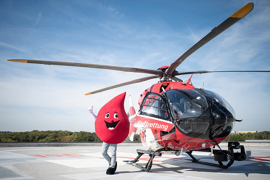 Ein Rettungshubschrauber steht auf dem Hubschrauberlandeplatz des Universitätsklinikums Halle (Saale). Daneben steht das Maskottchen der Blutspende und streckt die Arme in die Höhe. Ein Rettungshubschrauber steht auf dem Hubschrauberlandeplatz des Universitätsklinikums Halle (Saale). Daneben steht das Maskottchen der Blutspende und streckt die Arme in die Höhe.