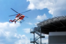 Ein rot-weißer Rettungshubschrauber fliegt in der Nähe der Hubschrauberlandeplatt-form des Universitätsklinikums Halle (Saale). Von der Plattform führt eine Treppe nach unten.