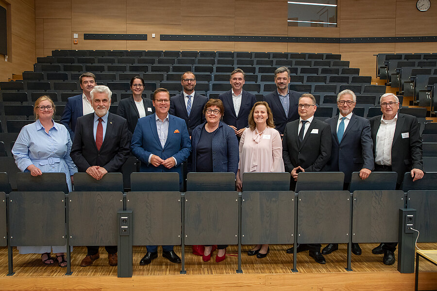 Dreizehn Menschen in zwei Reihen vor einem leeren Hörsaal stehen zusammen. Dreizehn Menschen in zwei Reihen vor einem leeren Hörsaal stehen zusammen.