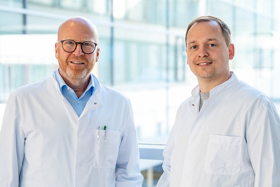 Zwei Männer stehen in einem Gang des Universitätsklinikums Halle (Saale) und schauen in die Kamera. Beide tragen Arztkittel. Zwei Männer stehen in einem Gang des Universitätsklinikums Halle (Saale) und schauen in die Kamera. Beide tragen Arztkittel.